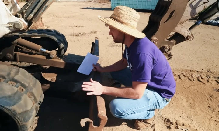 A man in a straw hat inspects machinery while taking notes, emphasizing maintenance for golf cart lithium batteries.