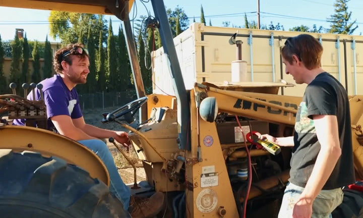 Two men work on a yellow tractor, discussing maintenance, highlighting the importance of reliable golf cart batteries.