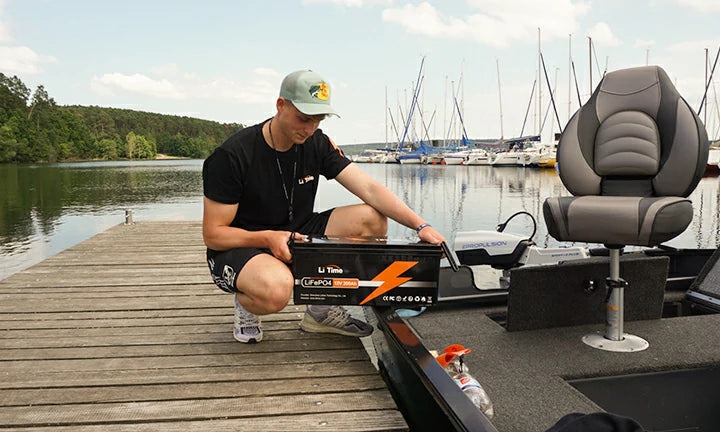 An angler kneels on a dock, setting up his bass boat's trolling motor and electronics