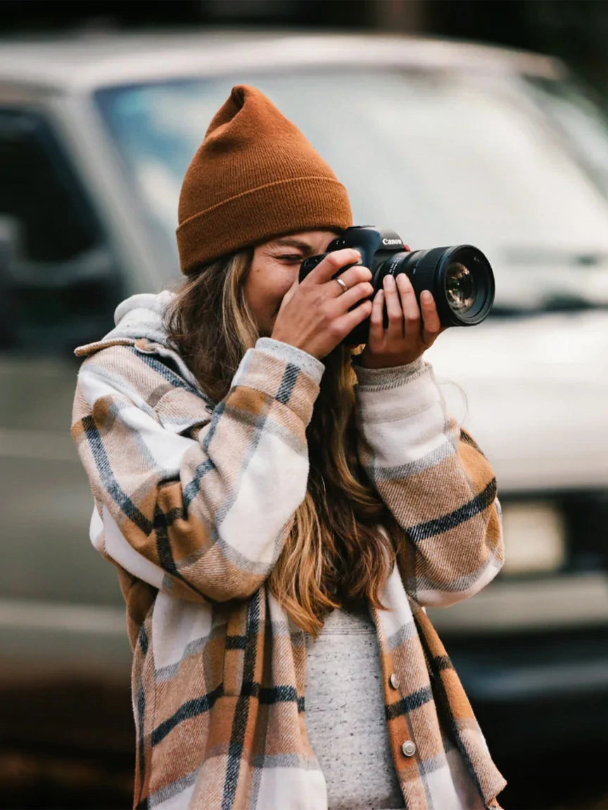 A woman in a beanie taking a photo with a professional camera, representing the LiTime blog and user adventure stories