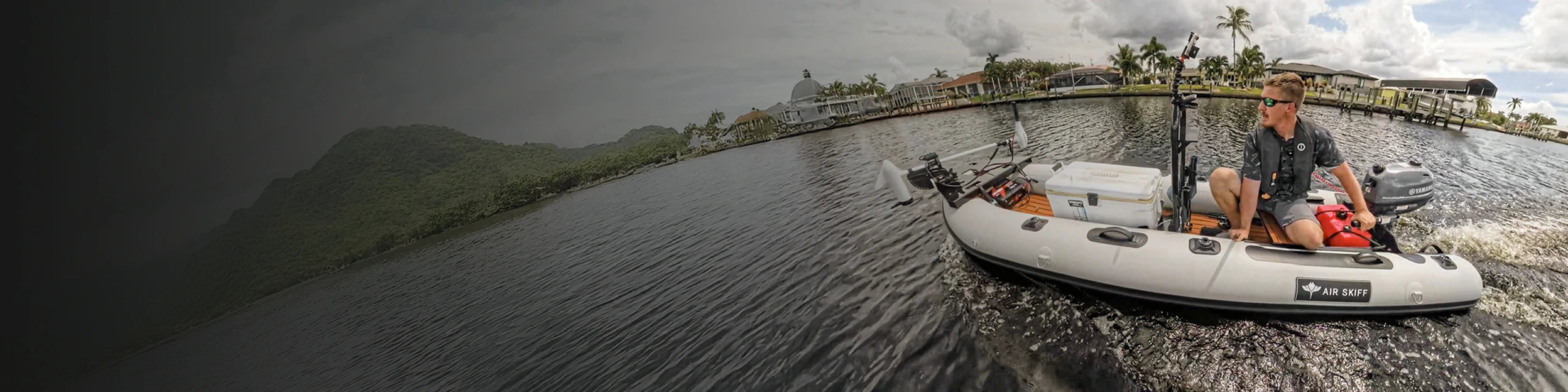 A young man pilots an inflatable sport canoe with a trolling motor through a calm, tropical waterway