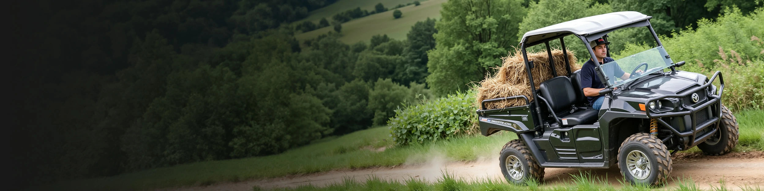 A man driving a black utility vehicle loaded with hay bales on a dirt path, showcasing golf cart battery capabilities.