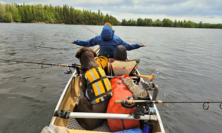 A couple and their dog enjoy a relaxing day of fishing from their canoe on a vast lake